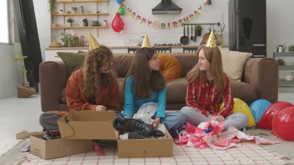 兴奋而又可爱的少女生日女孩坐在地板上 与戴着派对礼帽的快乐的少女朋友一起打开礼品盒 被生日礼物惊呆了 并拥抱了家中的朋友 — 图库视频影像