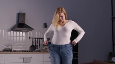 Neşeli, pozitif, bol kotlu olgun bir kadın. Yurt odasında duruyor. Başarılı kilo verme diyetinin başarısını gösteriyor ve dans hareketleri yapıyor.