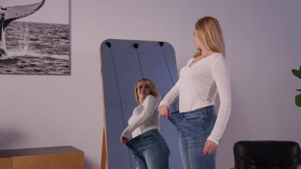 穿着太大牛仔裤的快乐迷人的成熟女人 看着镜子里的倒影 展示并享受减肥减肥的成就 在家里表达兴奋和快乐 — 图库视频影像