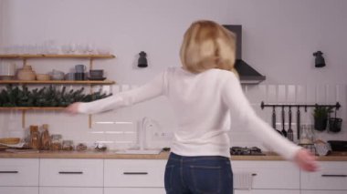 Keyifli, orta yaşlı, günlük giysiler içinde güzel bir kadın keyfine bakıyor, etrafta dönüyor ve ev mutfağındaki başarılı kilo verme programından sonra vücut şekillerini gösteriyor..