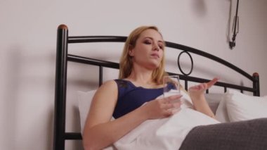 Uyku bozukluğundan muzdarip yetişkin bir kadının portresi. Yatmadan önce yatak odasında yatarken ilaç içip su içmesi..