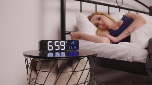 睡眠の怠惰な魅力的な成熟した女性が到達し 朝の夜のスタンドでデジタルアラーム時計をオフにし 警報信号を無視し 寝室で眠り続けます クローズアップ — ストック動画