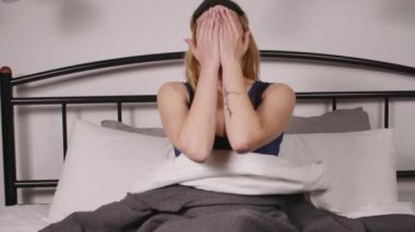 Huzurlu, uykulu, orta yaşlı bir kadın yatakta oturuyor, kollarını açıyor, esniyor ve gece rahat bir yatakta dinlenirken göz maskesi takıyor..