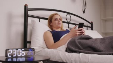 Yatakta uzanan, cep telefonuyla sosyal medya içeriğini internetten tarayan, yatak odasında uyumadan önce boş vakitlerin tadını çıkaran, gece kıyafetli, pozitif, rahat, olgun bir kadın..