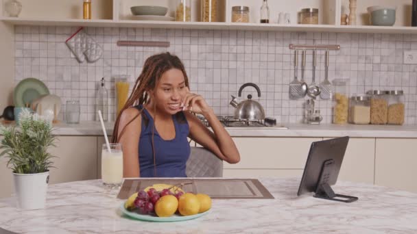 穿着睡衣坐在厨房桌旁 喝着健康的软饮料 在数字平板电脑上直播娱乐节目 同时在家里早上放松下来的快乐迷人的非洲裔美国女人 — 图库视频影像