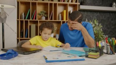Çekici Afrikalı Amerikalı babayı önemsemek okul ödevlerini kontrol etmek ve açıklamak, akıllı okul çağındaki oğlunun ödevlerini yapmasına yardım etmek aile odalarında birlikte okurken,