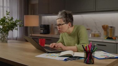 Gözlüklü, kafası karışık, çekici orta yaşlı iş kadını bilgisayardaki mali verileri ve açıklamaları kontrol ediyor ve analiz ediyor..
