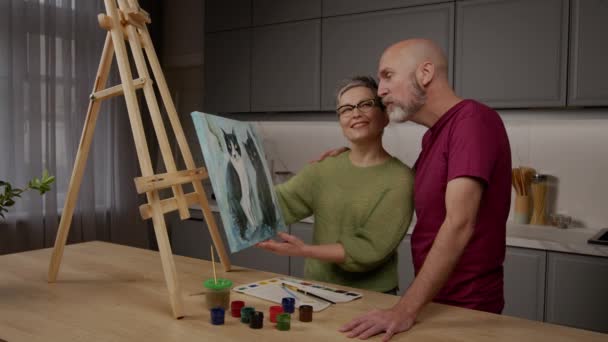 有才华的漂亮而成熟的女画家向中年男子展示油画 在享受家庭休闲的同时 讨论和交流对绘画的批判性意见 — 图库视频影像