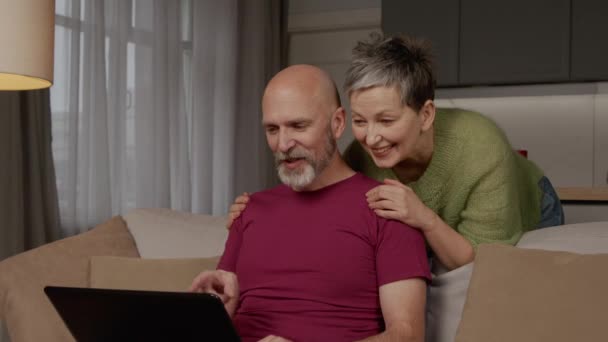 无忧无虑地放松迷人的胡子成熟男人和快乐可爱的中年女人在笔记本电脑上建立关系网 在网上观看有趣的视频内容 在家里放松的时候表达积极和快乐 — 图库视频影像