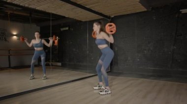 Ağırlık antrenmanı yapan, halter egzersizi yapan, bacak ve vücut kaslarını güçlendiren, iç mekan egzersizleri sırasında duruş ve hareketliliği geliştiren kararlı ve formda bir kadının yan görüntüsü.