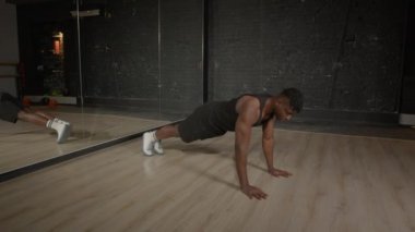 Motive edilmiş aktif spor formundaki Afrikalı adam bacak kenarı çıtırtısı ile ileri seviye şınav egzersizi yapıyor, spor yaparken üst ve alt vücut kaslarını güçlendiriyor..