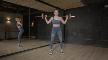 Spor kıyafetleriyle, ağırlık çalışması yaparak, halter egzersizleri yaparak, alt gövdeyi güçlendirerek, kalça kaslarını ve kuadriseps 'i hedef alarak motive olmuş, zayıf ve çekici bir kadın. Sağlık kulübünde.