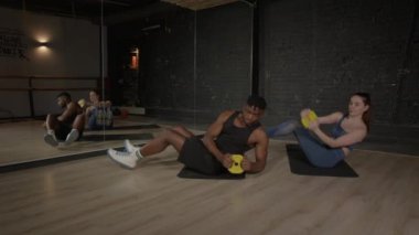 Etkin sportif kas yapısı siyah adam ve güzel bayan fitness antrenörü birlikte antrenman yapıyorlar, ağırlık plakası dönüş egzersizlerini yoga minderleri üzerinde yapıyorlar.