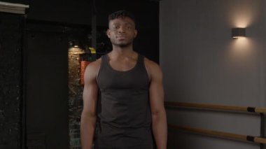 Pozitif yakışıklı, kaslı Afrikalı bir adam. Çift pazı pozisyonunda poz veriyor. Neşeli bir gülümsemeyle bakıyor..