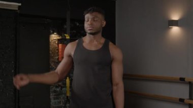 Aktif giyimli, kaslı, kaslı, ayakta duran ve pazılarını gösteren, neşeli bir gülümsemeyle bakan, gücünü, erkekliğini ve fitness kulübüne olan güvenini ifade eden yakışıklı, güçlü bir sporcunun portresi..