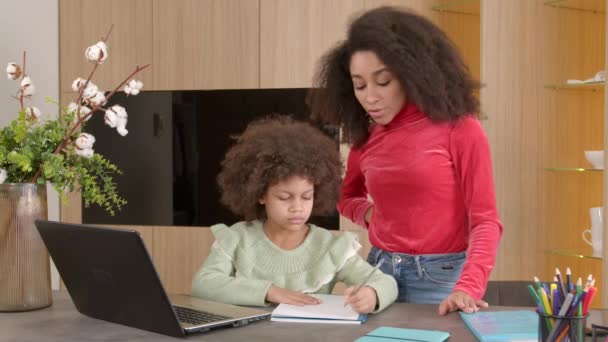 魅力的なアフリカ系アメリカ人の母親は 家事でかわいい学校の年齢の娘を助け 教材をチェックし 説明しながら 家庭で前向きな家族の学習を支援しています — ストック動画