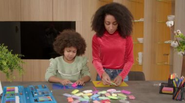 Neşeli Afro-Amerikan anne ve tatlı ilkokul çağında kıvırcık kız eğleniyor ve birlikte eğleniyor renkli oyun hamurlarından el işi oyuncaklar yaratıyor..