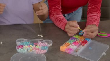Çocuk ve anne eli renkli boncuklardan ve lastik bantlardan çocuklar için ucuz el yapımı mücevherler yapıyorlar..
