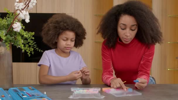 积极迷人的非洲裔美国母亲和快乐可爱的小毛茸茸的女儿一起享受着娱乐活动 用彩色珠子和橡皮筋为孩子们做了手工珠宝 — 图库视频影像