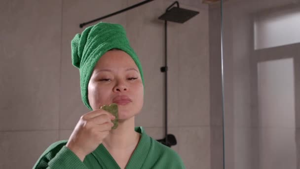 美容美发的亚洲中年女子头戴浴衣 在浴室用翡翠面部按摩工具进行温泉疗养及面部整容的肖像 — 图库视频影像