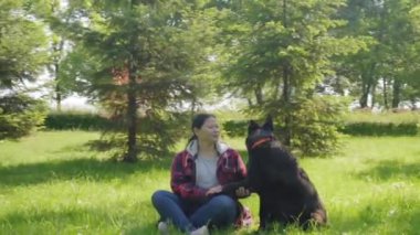 Sevecen, sevimli, safkan, Doğu Avrupa 'lı zenci dişi çoban köpeği. Mutlu, orta yaşlı Asyalı kadın köpek sahibine patisini veriyor. Yaz parkında güven, güçlü bir bağ ve dostluk gösteriyor..
