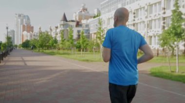 Aktif olarak belirlenen spor kıyafetleriyle koşan olgun erkek sporcuların arka görüntüsü, yükselen sıcak güneş ışınlarında kardiyo çalışması..