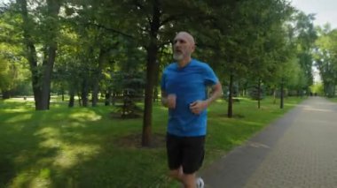 Aktif motive olmuş atletik olgun erkek koşucu göğüs ağrısı çekiyor, kalbi acı dolu bir ifadeyle tutuyor ve halk parkında yoğun sabah koşusu yaparken mola veriyor..