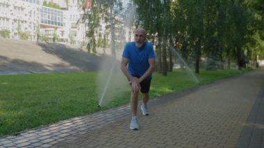 Motive olmuş sportif fit orta yaşlı adam bacak egzersizleri yapıyor, ısınıyor, kaslarını geriyor ve halka açık parkta koşmadan önce kaslarını kasıyor.