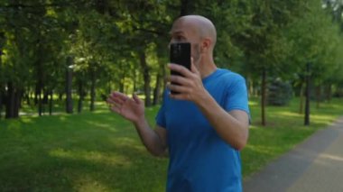 Aktif giyimli çekici orta yaşlı bir adam internetten video araması yapıyor cep telefonu kullanıyor, arkadaşlarıyla iletişim kuruyor ve her sabah spor yaparken parkta yürüyor..