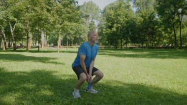 Spor kıyafetleri içinde orta yaşlı, çekici ve formda bir adam. Halterli sumo egzersizleri yapıyor. Yaz mevsiminde vücut gücünü arttırıyor..