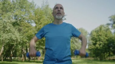 Kararlı sportif formda olgun bir adam. Düz sıra halterler, trapezius ve trisepsleri güçlendirerek açık hava sporları antrenmanı yapıyor..