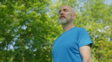 Spor formalı, yakışıklı, sakallı, orta yaşlı bir adamın portresi. Boş zamanların tadını çıkarıyor, temiz hava soluyor, yaz doğasında dururken mutluluk ve pozitifliği ifade ediyor..