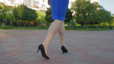 :Çekici, zayıf, orta yaşlı, şık siyah topuklu ayakkabılı kadın bacaklarının arka manzarası yaz günü yaya caddesinde yürüyor. Düşük açı. Yakın plan..