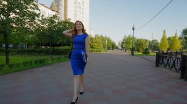 Başarılı kızıl saçlı, olgun, şık topuklu ayakkabılar ve elbiseler giyen, elinde not panosu ve dijital tabletle şehir caddesinde yürüyen, kendine güvenini ifade eden, başarılı bir girişimci.