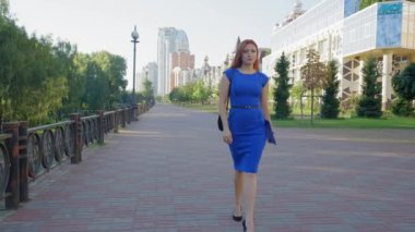 Zarif, kızıl saçlı, orta yaşlı, şık topuklu bir bayan girişimci, ayak bileğini burkmuş, acı içinde caddede yürürken ayağına dokunuyor.,