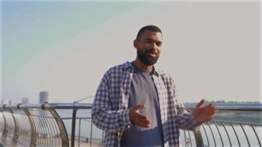 Olumlu çekici sakallı Afrikalı Amerikalı erkek blogcu canlı yayın vlog 'u, güneşli bir yaz gününde şehir sokaklarında yürürken çevrimiçi izleyicilerle iletişim ve paylaşım yapıyor.