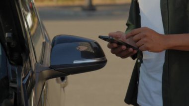 Close-up of black male driver hands browsing online on cellphone , searching for roadside assistance service near broken car while travelling by vehicle in city.