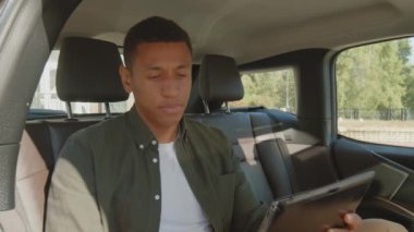 İş gezisi sırasında tablet bilgisayarla çalıştıktan sonra yorgun gözlerle araba koltuğunda dinlenen, şık giyinen, aşırı çalışkan, çekici siyah iş adamı aşırı yüklenmiş ve yorgun hissediyordu..