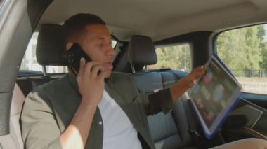 Başarılı bir Afrikalı Amerikalı erkek yönetici. İş seyahatinde arabasıyla arka koltukta seyahat ediyor, iş arkadaşıyla cep telefonuyla konuşuyor ve finansal verileri tartışıyor.