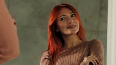 Mutlu kızıl saçlı orta yaşlı kadın portresi aynada yansımaya bakıyor, güzellik makyajını ve görünüşünü kontrol ediyor, evde keyif ve güven ifade ediyor..