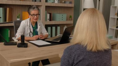 Üniformalı, çekici, olgun bir kadın doktor. Doğum öncesi kliniğinde hamilelik ve hamilelik konusunda danışmanlık yapan mutlu hamile bir kadına ultrason görüntüsü veriyor..