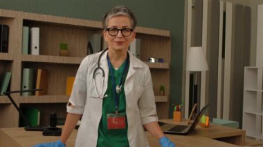 Üniformalı ve koruyucu eldivenli, kolları kavuşturulmuş bir kadın pratisyen doktorun portresi güven ve pozitifliği ifade ediyor..