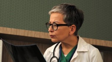 Kafası karışmış profesyonel kadın doktorların portresi insan omurgasının röntgen görüntüsünü analiz ediyor, tedaviyi düşünüyor, tıbbi klinikte çalışırken omurilik bozulması endişesini dile getiriyor..