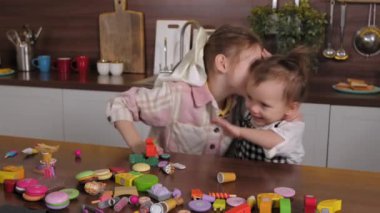 Neşeli, sevimli, ilkokul çağında abla neşeli küçük kızı kucaklıyor, sevgi ve mutluluk gösterirken pozitif çocuklar evcil odada renkli oyuncaklarla oyun oynuyorlar..