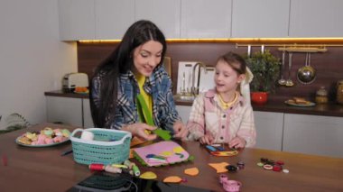 Sevimli, sevimli okul kızı ve ilgili güzel anne çocukların çantalarını hazırlıyor, dekoratif süsler dikiyor, iğne iplik takıyor ve aile evde boş vakitlerin tadını çıkarıyor..