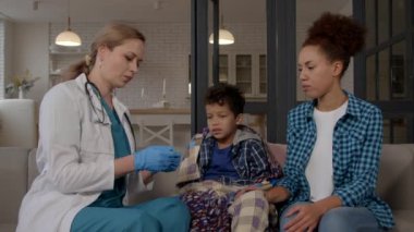 Üniformalı kadın pratisyen doktor sağlık kontrolü yapıyor, hasta okul çağındaki yüksek ateşi olan Afrikalı Amerikalı çocuğun sıcaklığını ölçüyor ve endişeli annesine çocuk sağlığı durumundan bahsediyor..