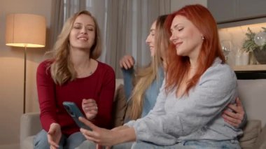 Neşeli bayan arkadaşlar eski sınıf arkadaşları okul buluşması için buluşuyor, cep telefonunda selfie çekimi için poz veriyor, neşeli ruh halini ve ev ortamında mutluluğu ifade ediyor..