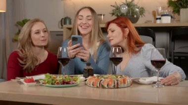 Orta yaşlı kadınların yemek masasında toplanıp sosyal medya için cep telefonuyla lezzetli suşi ve taze salata videoları çekmeleri ve evde eğlenmeleri..