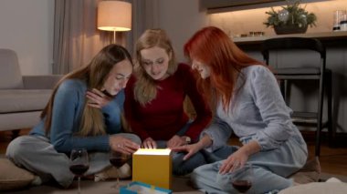 Şaşırmış, çekici orta yaşlı kadınlar yerde oturuyor, hediye kutusuna merakla bakıyor, evde doğum günü partisini kutlarken parlak ışık yüzlerini aydınlatıyordu..
