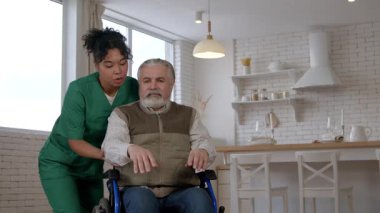 Afrikalı Amerikalı kadın bakıcı üniformalı yaşlı, gri saçlı, yaşla ilgili hareket engelli bir adama yardım ediyor, bakım evindeki kol kaslarını güçlendirmek için egzersiz yapıyor..